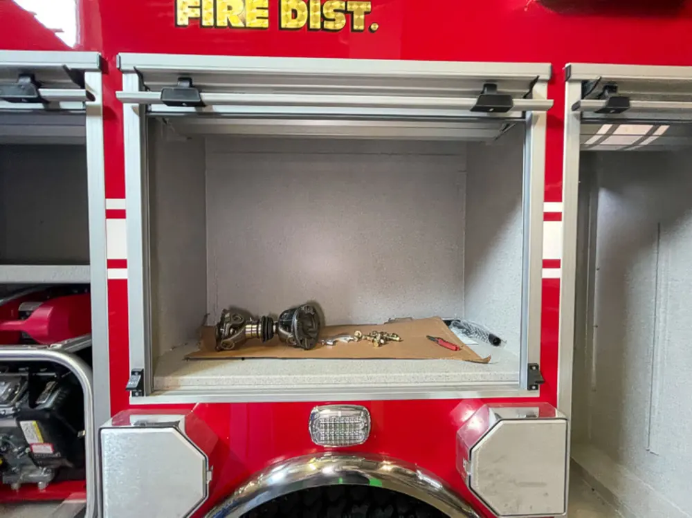 Exterior view of small fire truck showing cab, body compartments, and wheel/tire area.